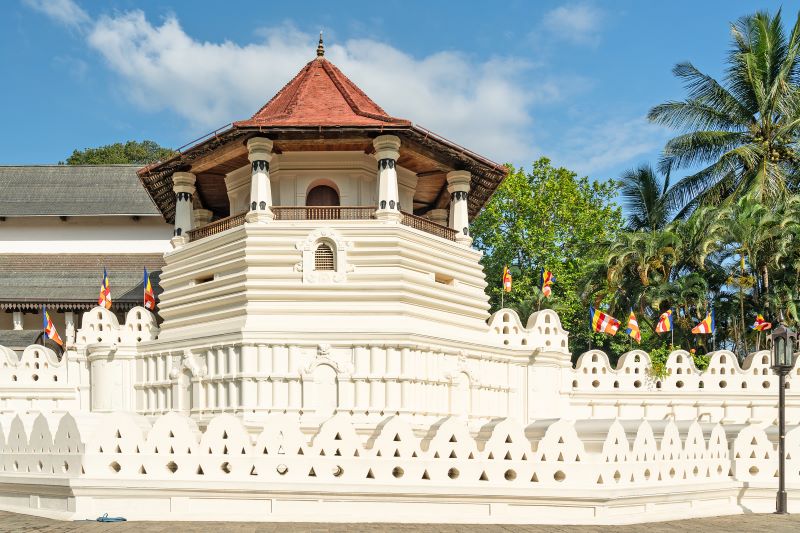 biele múry chrámu budhovho zubu s vezickou a cervenou strechou v kandy