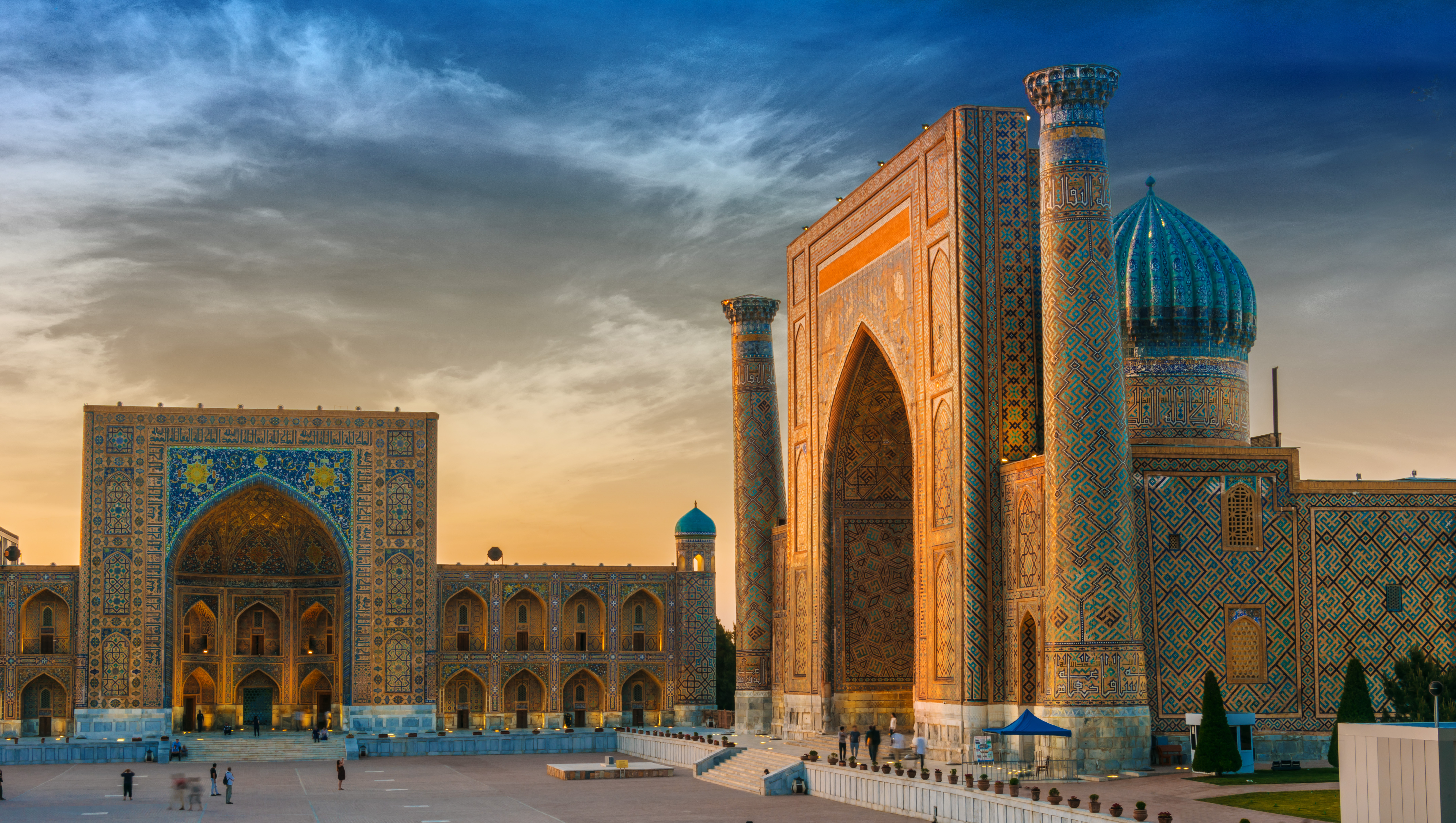 Návštevníci medzi mauzóleami s modrými a tyrkysovými mozaikami v komplexe Šáh-i-Zinda v Samarkande, Uzbekistan.